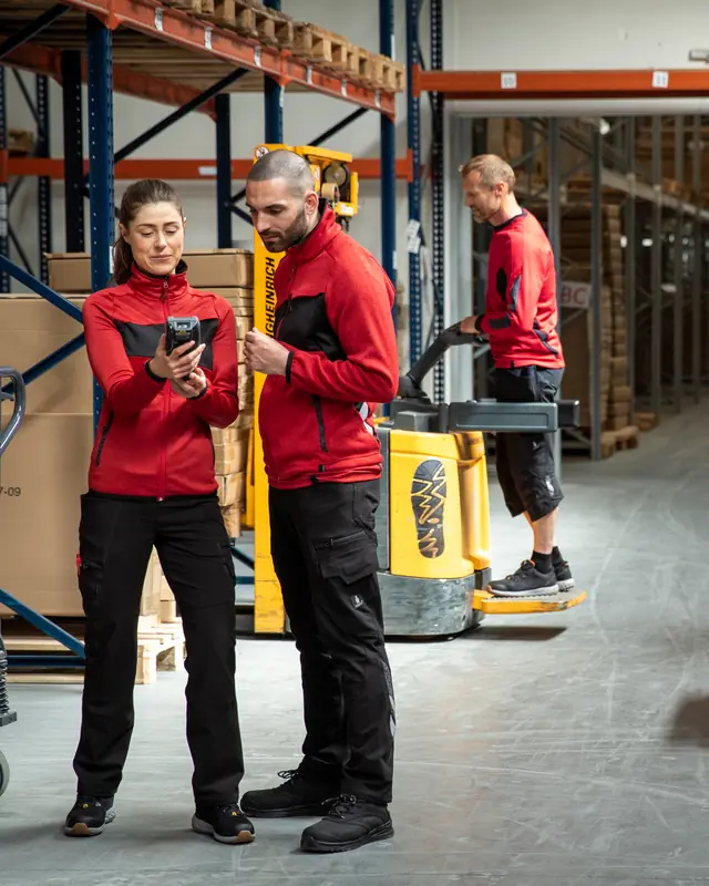 Lagerteam in roter MASCOT ACCELERATE Arbeitskleidung mit Hubwagen im Hochregallager